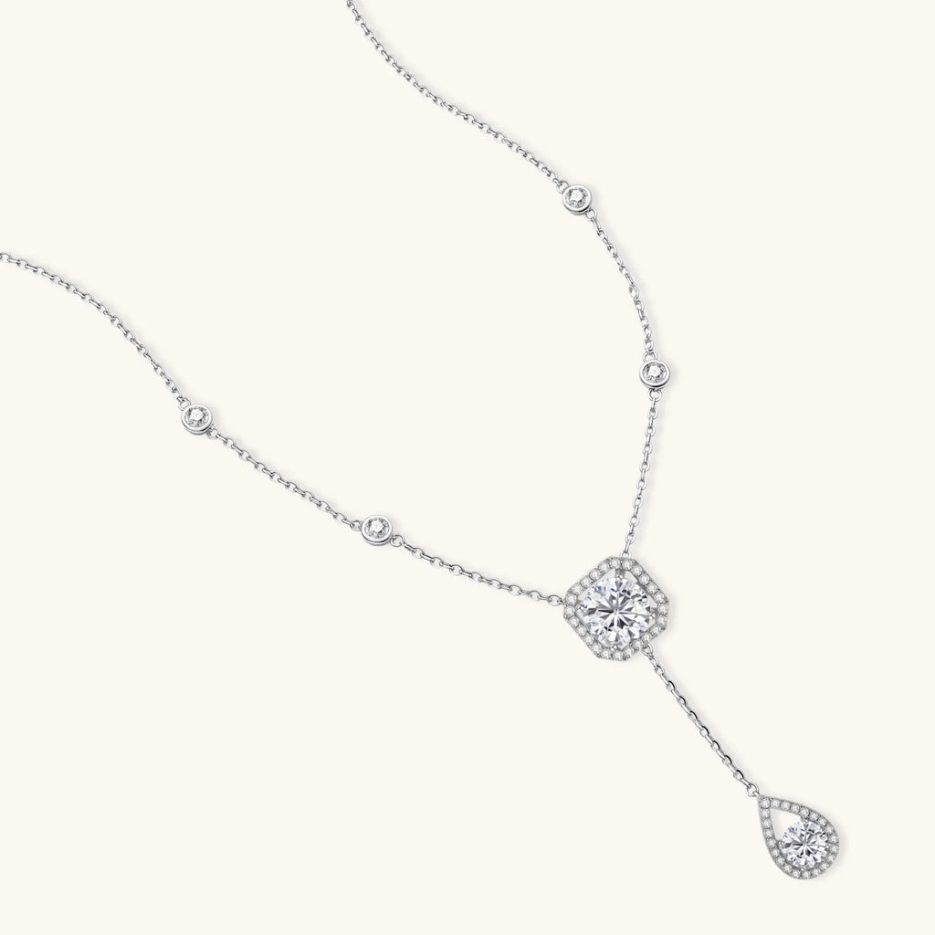 Sterling silver necklace with cushion-cut moissanite in halo setting and teardrop pendant, displayed on cream background.