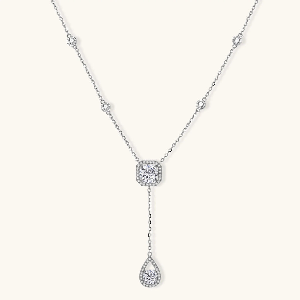 Sterling silver necklace with cushion-cut moissanite in halo setting and teardrop pendant, displayed on cream background.