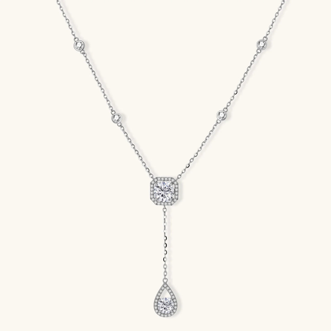 Sterling silver necklace with cushion-cut moissanite in halo setting and teardrop pendant, displayed on cream background.