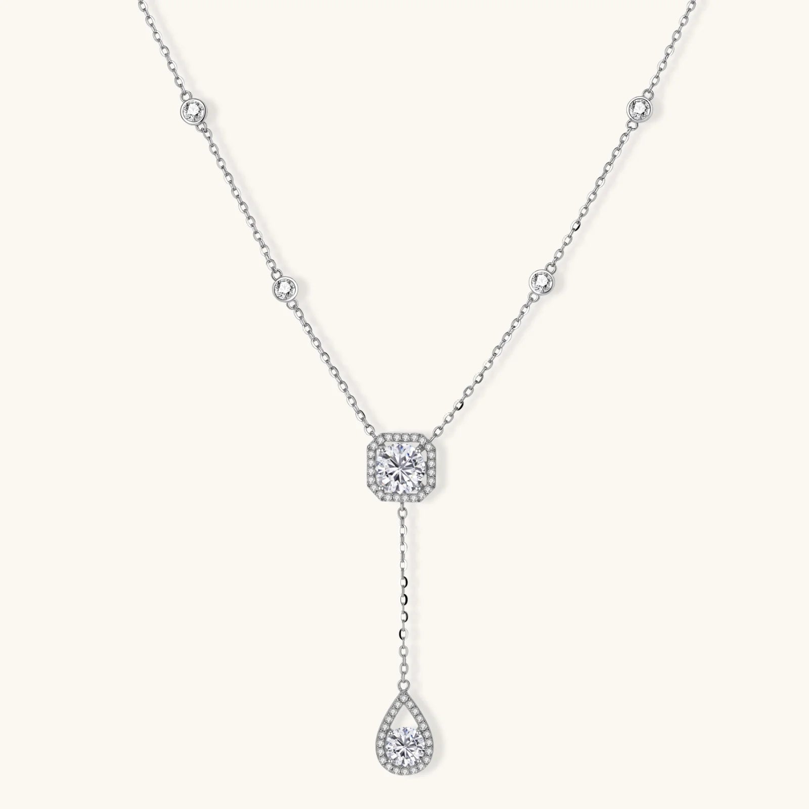 Sterling silver necklace with cushion-cut moissanite in halo setting and teardrop pendant, displayed on cream background.
