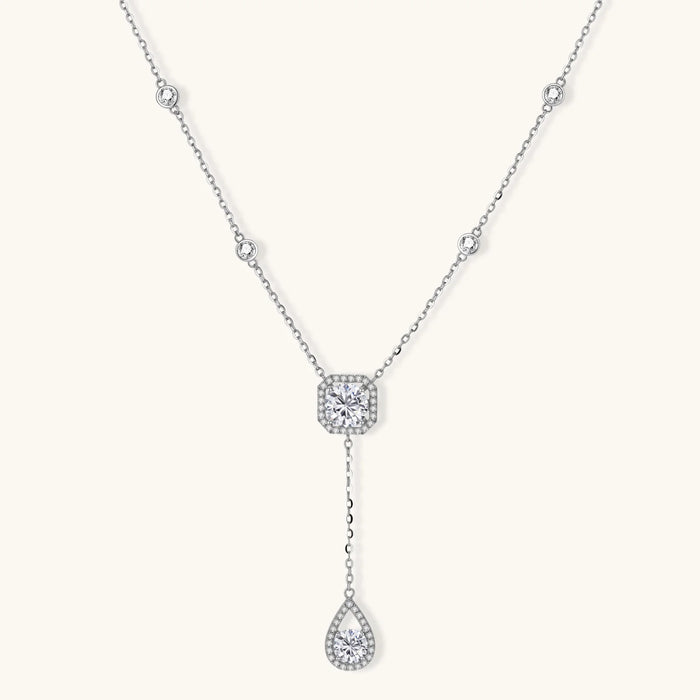 Sterling silver necklace with cushion-cut moissanite in halo setting and teardrop pendant, displayed on cream background.