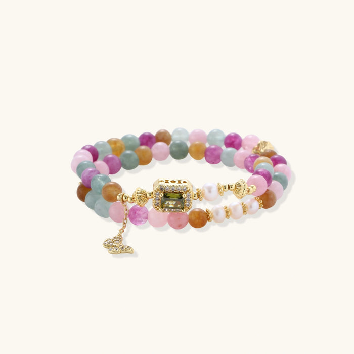 Stretchable bracelet with pastel gemstone beads, freshwater pearls, gold centerpiece and butterfly charm on cream background