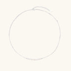 Delicate sterling silver chain necklace with small freshwater pearls arranged in a curved smile arc on cream background.