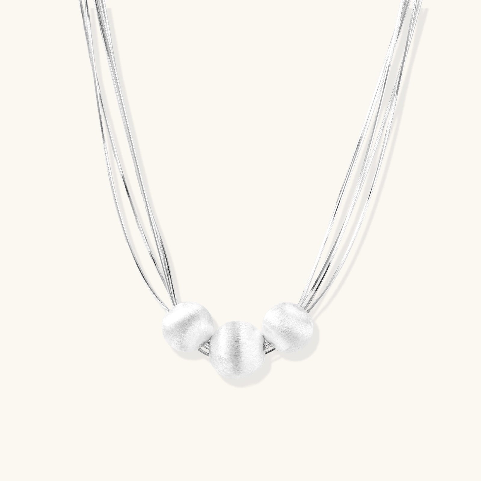 Sterling silver multi-strand necklace with three brushed round beads on cream background