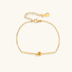 Delicate gold chain bracelet with minimalist bar and centered knot detail on cream background