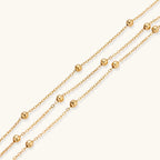 Three-strand gold-plated bracelet with clustered ball beads and adjustable clasp on cream background