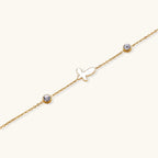 Gold chain bracelet with white mother of pearl butterfly pendant and two bezel-set crystals on cream background