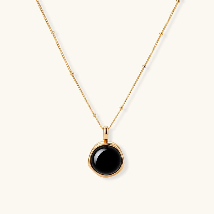 Circular black agate pendant on gold-plated sterling silver chain against cream background, showing modern minimalist design.