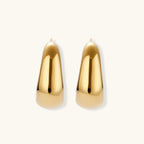 Close-up of curved gold-plated huggie earrings with sculptural design on white background, showing polished finish.