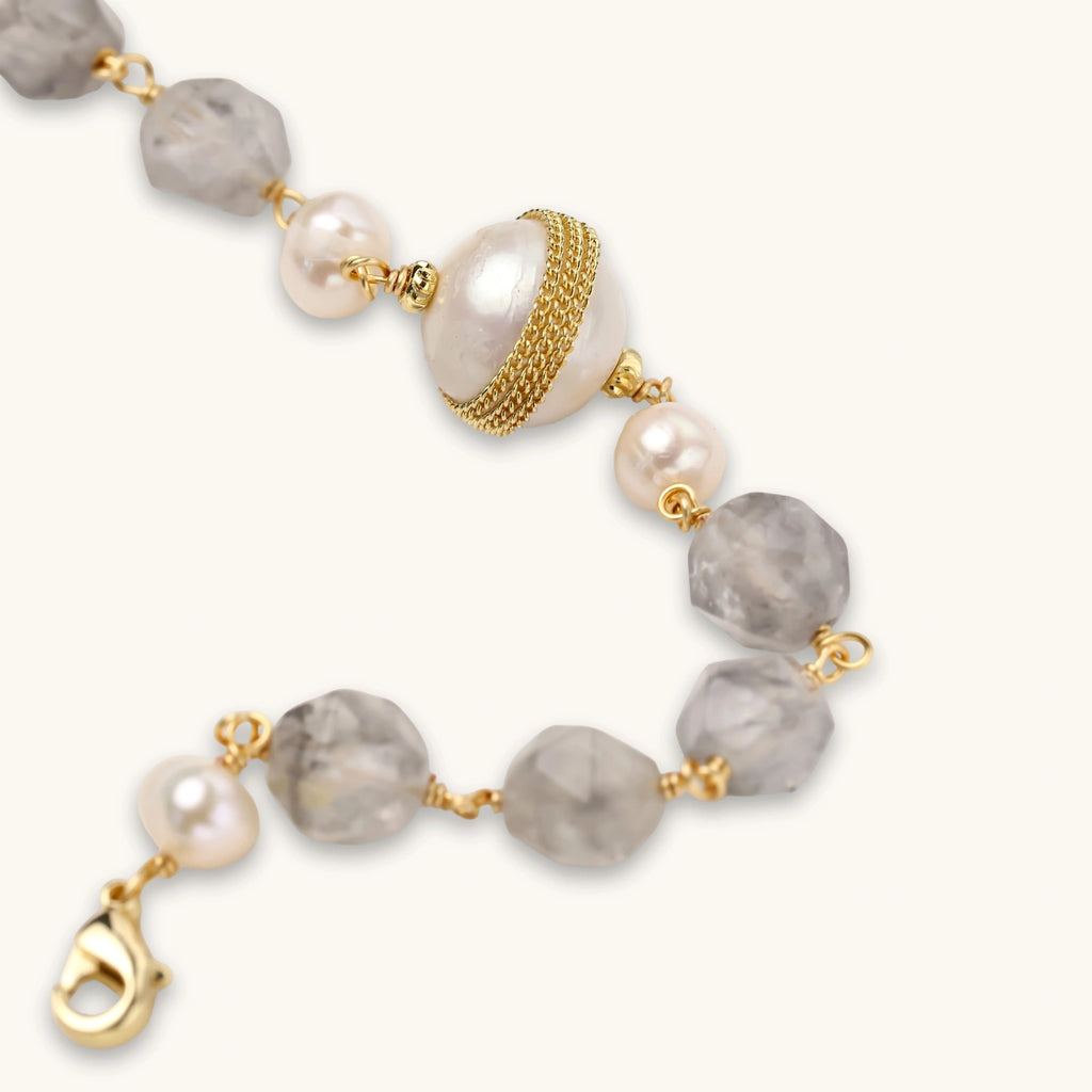 Bracelet with cloudy quartz beads, freshwater pearls, and gold-wrapped baroque pearl centerpiece on white background.