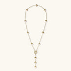 Gold-plated lariat necklace with baroque pearls and textured caps on cream background, showing adjustable Y-shaped design.