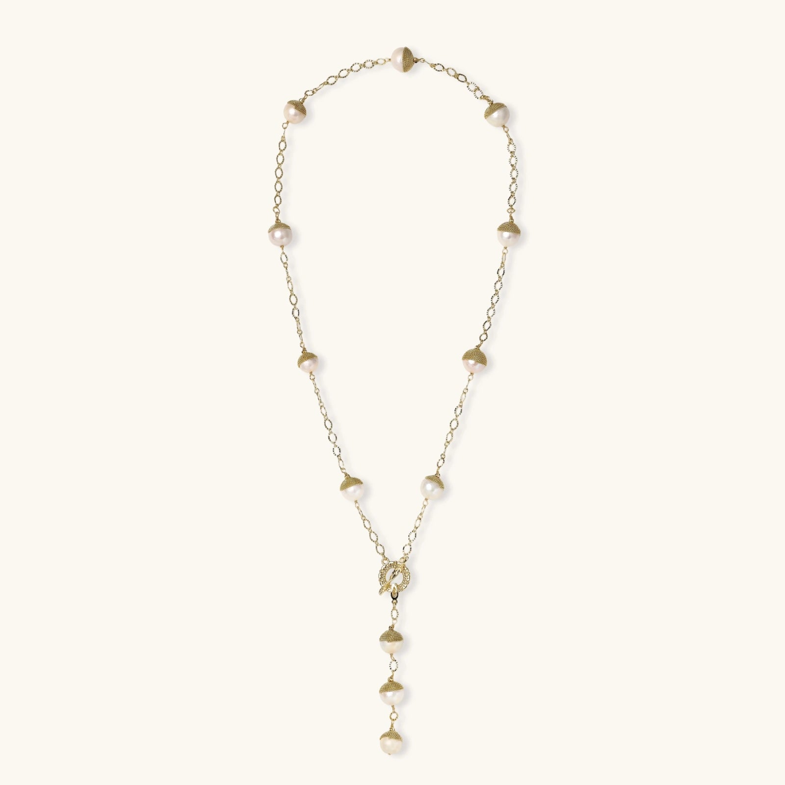 Gold-plated lariat necklace with baroque pearls and textured caps on cream background, showing adjustable Y-shaped design.