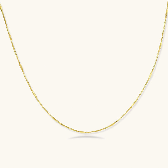 Delicate gold-plated sterling silver chain necklace with geometric segments displayed against cream background
