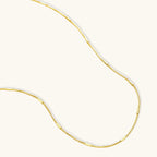 Delicate gold-plated sterling silver chain necklace with geometric segments displayed against cream background