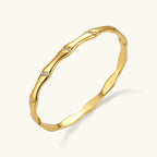 Gold-toned wavy bangle with bamboo-style segments and CZ crystal clusters on cream background. 18K plated stainless steel.