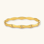 Gold-toned wavy bangle with bamboo-style segments and CZ crystal clusters on cream background. 18K plated stainless steel.
