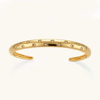 Polished 18K gold plated cuff bracelet with cubic zirconia set in star motifs on a cream background.